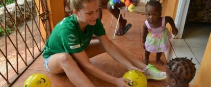A Projects Abroad high school student volunteer plays a game with children in Jamaica at her placement. A volunteer working with children at a Summer Camp in Jamaica, leads a ball activity at her placement.